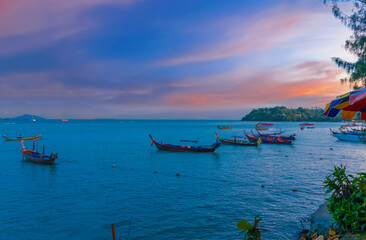 Colourful Skies Sunset over Rawai Beach in Phuket island Thailand. Lovely turquoise blue waters, lush green mountains colourful skies and beautiful views the pier and longtail boats and islands 