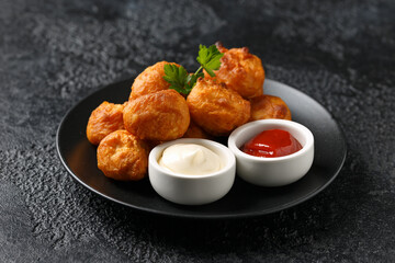 Battered chicken balls with tomato ketchup, mayonnaise on black plate. Party food