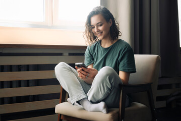 Connected and Productive: Young Woman Embraces Technology, Engaging in Communication and Studies Using Smartphone at Home. A Modern Lifestyle Balancing Work, Study, and Connection Through Mobile Apps