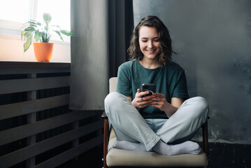 Obraz premium Digital Lifestyle: Young Woman Engages in Communication and Productivity Through Smartphone in the Comfort of Home. A Blend of Study, Work, and Connection in the Digital Age.