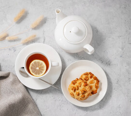 Tea with lemon in a white cup on a light background with homemade cookies and a teapot. The concept of a healthy and tasty breakfast.