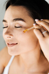 Young woman with acid dropper is applying drops of acid on her skin. Girl applying hyaluronic serum...