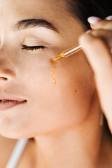 Attractive girl drops essential oil on facial skin close-up. Young woman is applying moisturizing...