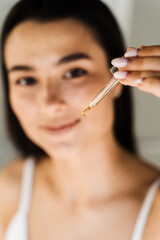 Attractive girl with drop of essential oil in pipette in hands close-up. Young woman is applying moisturizing serum on her skin.