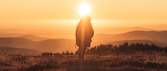 Woman walking on a mountains peak when sun is going down, beautiful sunset in Krkonose, Czech republic