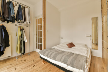 a bedroom with wood flooring and white walls, there is a large bed in the room has a mirror hanging on the wall