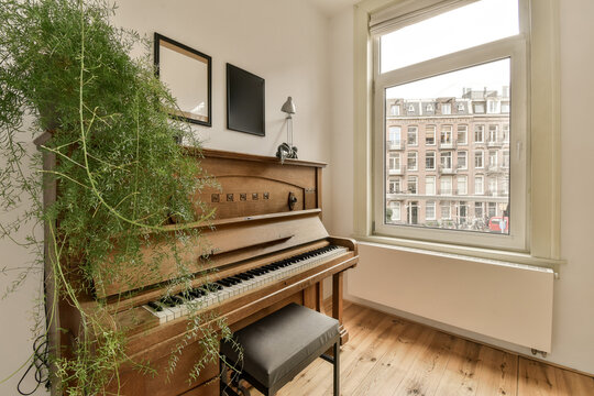 a living room with an old piano and some plants in the window simng it's white walls