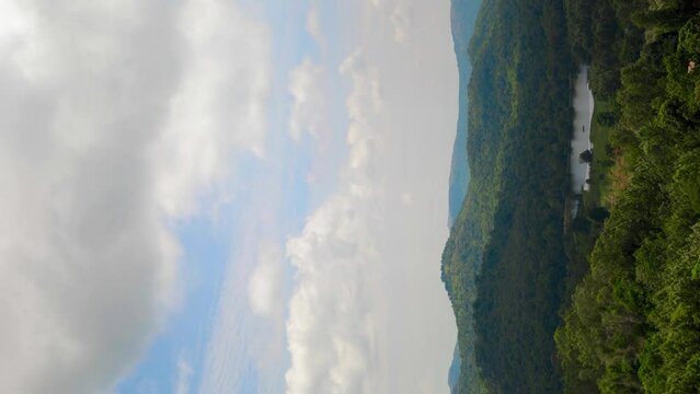 time lapse of a hilly area with trees and a pond - clouds moving in the sky casting shadows