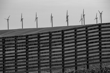 Nine wind turbines line a ridge behind a wooden fence. 