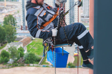 Professional climber rope access worker painting, repairing and cleaning windows on the facade of...