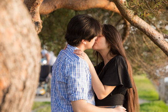 Attractive biracial young couple kissing under pine trees