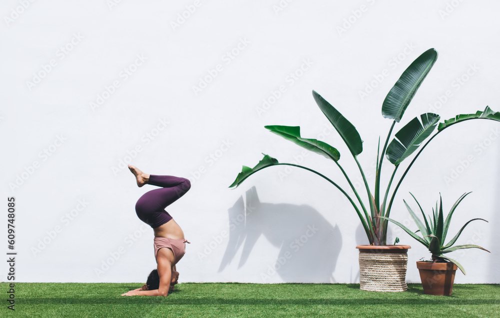 Wall mural strong female in casual sportive wear standing in asana on artificial lawn stretching body and keepi