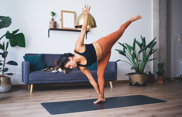 Motivated woman in track suit standing in hatha pose breathing and enjoying recreation at home apartment, female practice yoga mantras feeling inspiration in asana keeping body positive lifestyle