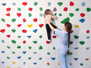 physiotherapist instructor helping little girl to climb wall in gym. sensory integration for kid and correctional physiotherapy to replenish sensory experience - obrazy, fototapety, plakaty