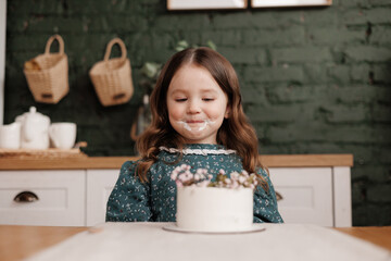 Adorable little child girl wears festive dress takes a bite out of a decorated flowers name cake at...