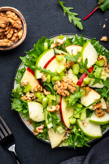 Waldorf salad with red and green apple, raw celery, lettuce, arugula and walnuts with mayonnaise dressing, black table background, top view