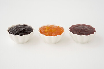 Three types of jam in white vases on a white background.