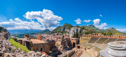 Taormina on Sicily, Italy. Ruins of ancient Greek theater, mount Etna covered with clouds. Taormina old town and mountains in background. Popular touristic destination on Sicily