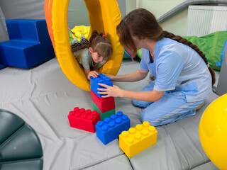 Child girl in roller tonnel during sensory integration session. child with physiotherapist in...