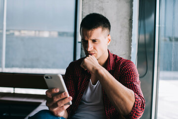 Focused man using smartphone while sitting near window
