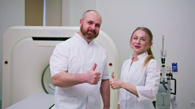 smiling and satisfied doctors in uniform posing near magnetic resonance imaging machine concept of professions and medicine