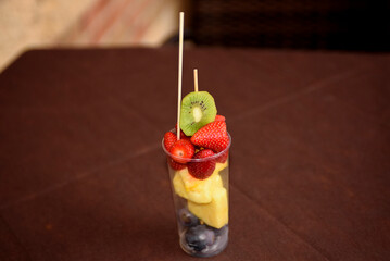 Assorted fruits in a glass on the table of a summer cafe. Summer dessert close-up.
