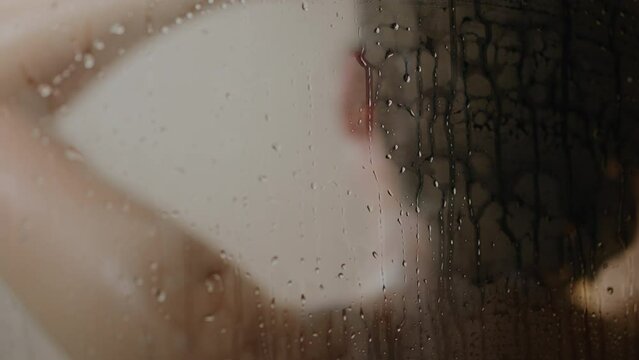 The girl takes a shower. Taking a hot rain shower in a city apartment, Close-up of body parts neck shoulders arms, Female body naked in a warm shower over a falling stream of water
