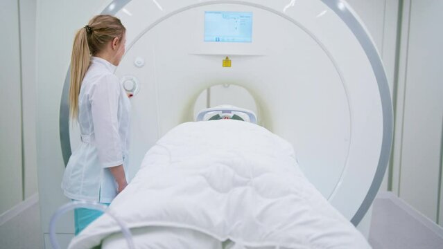 A professional radiologist in a medical clinic monitors a patient undergoing a magnetic resonance imaging procedure