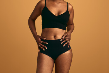 Crop black obese woman in underwear standing against beige background