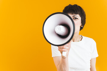 Medium shot of a young woman shouting into a loudspeaker. Bright yellow wall in the background. High quality photo