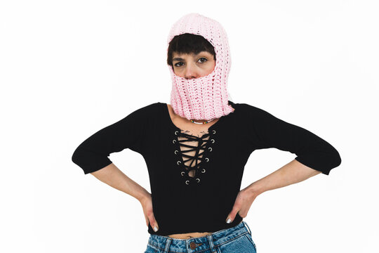 Young woman posing on a white background wearing jeans, a black top and a pink balaclava. High quality photo