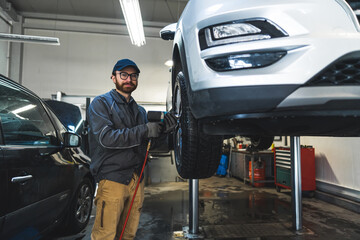 Naklejka premium Auto mechanic standing by the car on a lift and replacing a wheel with pneumatic wrench . High quality photo