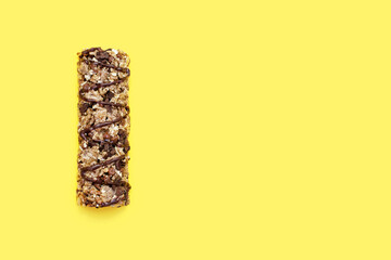 Muesli bar on a yellow background in the center. Whole grain energy bar with chocolate. Healthy food in the form of a sweet healthy bar. Healthy quick snack. Free space for text