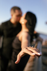 An engagement ring with a precious stone on the finger of a woman being kissed by her man. A young couple in love dressed in black and kissing at sunset. The man made a marriage proposal