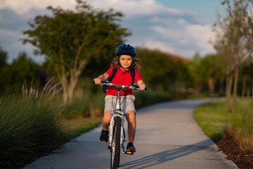 Naklejka premium Little kid boy ride a bike in the park. Kid cycling on bicycle. Happy smiling child in helmet riding a bike. Boy start to ride a bicycle. Sporty kid bike riding on bikeway. Kids bike.