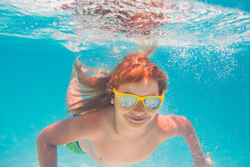 Kid swimming underwater. Summer kids. Happy little boy in swimming pool on summer day. Funny kid swimming and diving in pool. Kid underwater with splashes. Summer children water sports activity.