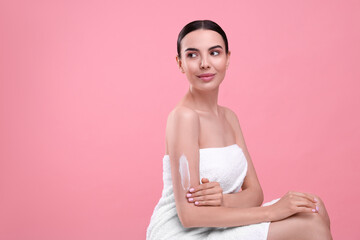 Beautiful woman with smear of body cream on her arm against pink background, space for text