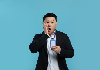 Emotional asian man with vip pass badge on light blue background