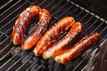 Cooking food in garden. On BBQ grill grate are fresh grilled traditional Nuremberg sausages, ready to be eaten - barbecue grilling outdoors in Germany