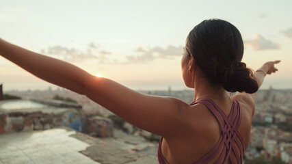Close up, young woman in bodysuit practices yoga at sunrise at viewpoint. Back view