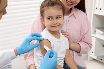 Children's hepatitis vaccination. Mother with her daughter in clinic. Doctor sticking medical...