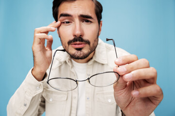 Close-up portrait of a man looking through glasses that he holds in his hands, dioptric lenses, glasses for far-sightedness and near-sightedness, on a blue background in a white T-shirt, copy space 