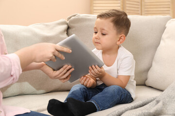 Internet addiction. Mother taking away tablet from her little son on sofa at home, closeup