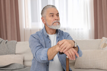 Senior man with walking cane sitting on sofa at home