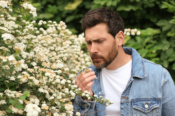 Man suffering from seasonal pollen allergy near blossoming tree on spring day