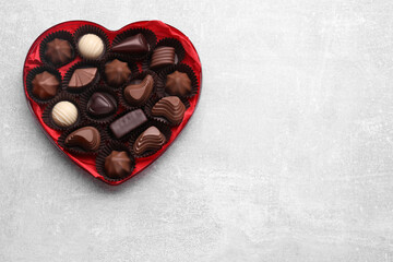 Heart shaped box with delicious chocolate candies on light grey table, top view. Space for text