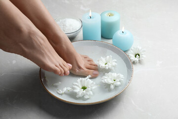 Woman soaking her feet in bowl with water and flowers on grey marble floor, closeup. Pedicure...