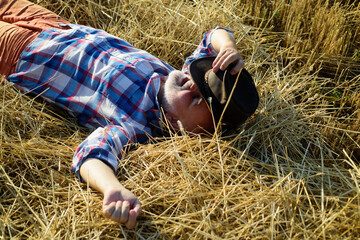 Old farmer in the hay. Senior relaxing on a straw hay on an summer day. Grandfather laying on haystack in countryside. Mature man resting at cereal field.
