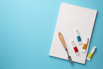 Blank canvas, tubes of oil paints and spatula on light blue background, flat lay. Space for text