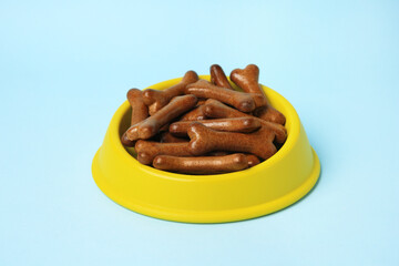 Yellow bowl with bone shaped dog cookies on light blue background, closeup